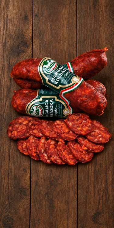 Ostra węgierska kiełbasa Palatin Mangalica Kolbászka, dojrzewająca i wędzona, w całości i w plasterkach na rustykalnym drewnianym tle. OstryStefek.pl.
