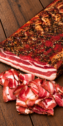 Palatin Feketekői kolozsvári Hungarian bacon, shown as a whole slab with thin slices on rustic wood. Explore Hungarian deli meats at OstryStefek.pl.