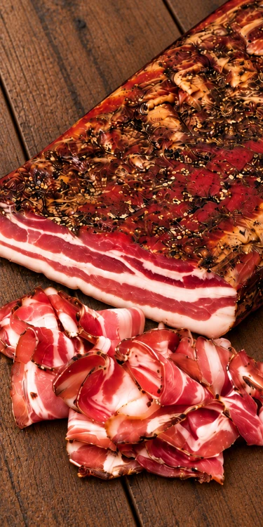 Palatin Feketekői kolozsvári Hungarian bacon, shown as a whole slab with thin slices on rustic wood. Explore Hungarian deli meats at OstryStefek.pl.