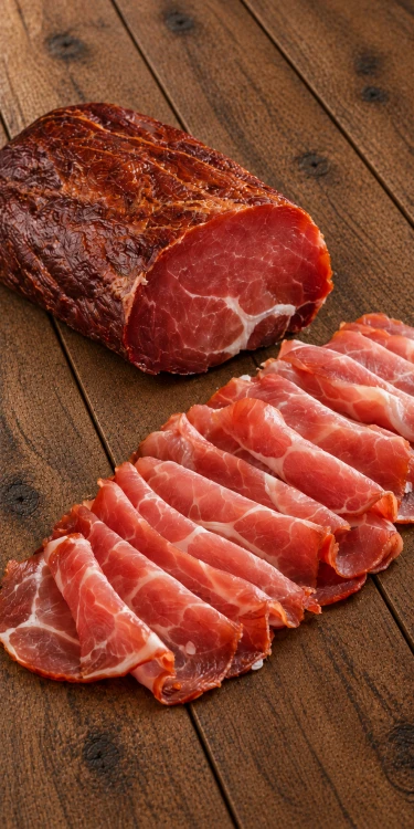 Pork loin shown whole and thinly sliced on rustic wooden planks. Explore Hungarian deli meats at OstryStefek.pl.