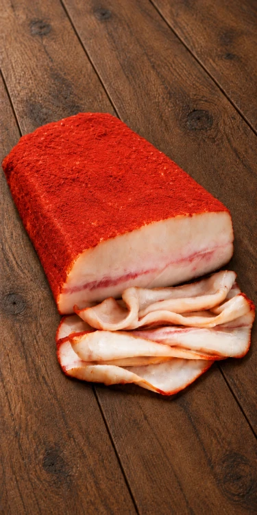 Smoked Mangalica pork fatback coated in ground paprika, with its cut face and thin slices displayed on rustic wooden boards.