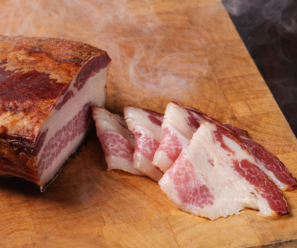 Dry-aged and smoked Mangalica bacon, Kolozsvár-style, presented on a wooden board with Hungarian red peppers and a light touch of smoke, highlighting the traditional smoking process. Premium Hungarian delicacy.