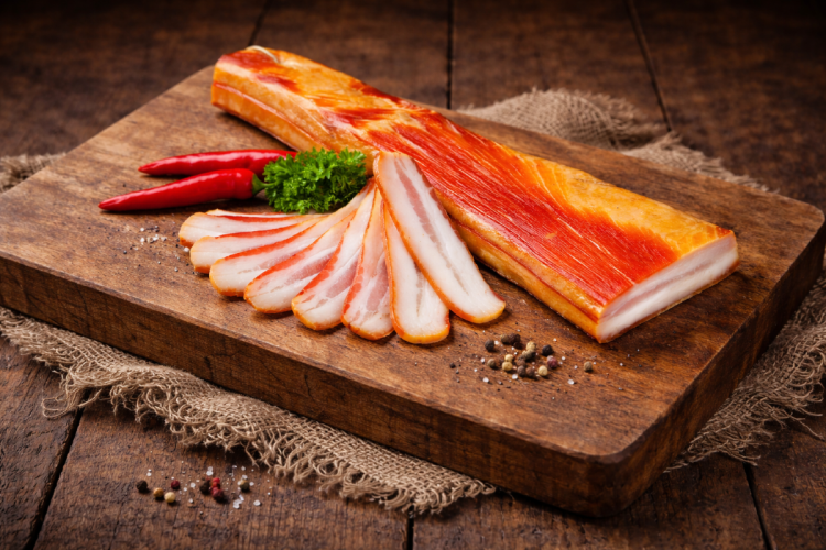 Thin-sliced smoked Hungarian bacon (szalonna) with a rich, savory aroma and delicate cured texture. Paper-thin slices served on a wooden board in a rustic, elegant setup—perfect for charcuterie boards and tasting plates.