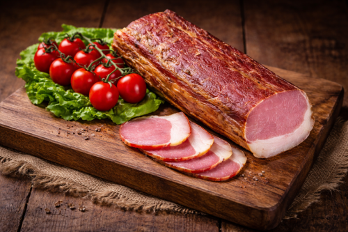 Dry-cured smoked pork loin presented in a rustic setting. Traditionally prepared, firm texture with a delicate fat layer. Perfect for sandwiches, charcuterie boards and premium cuisine.
