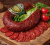 Traditional Hungarian dry-cured sausage served on a wooden board with sliced pieces, lettuce, and cherry tomatoes. Rich flavor and rustic presentation.